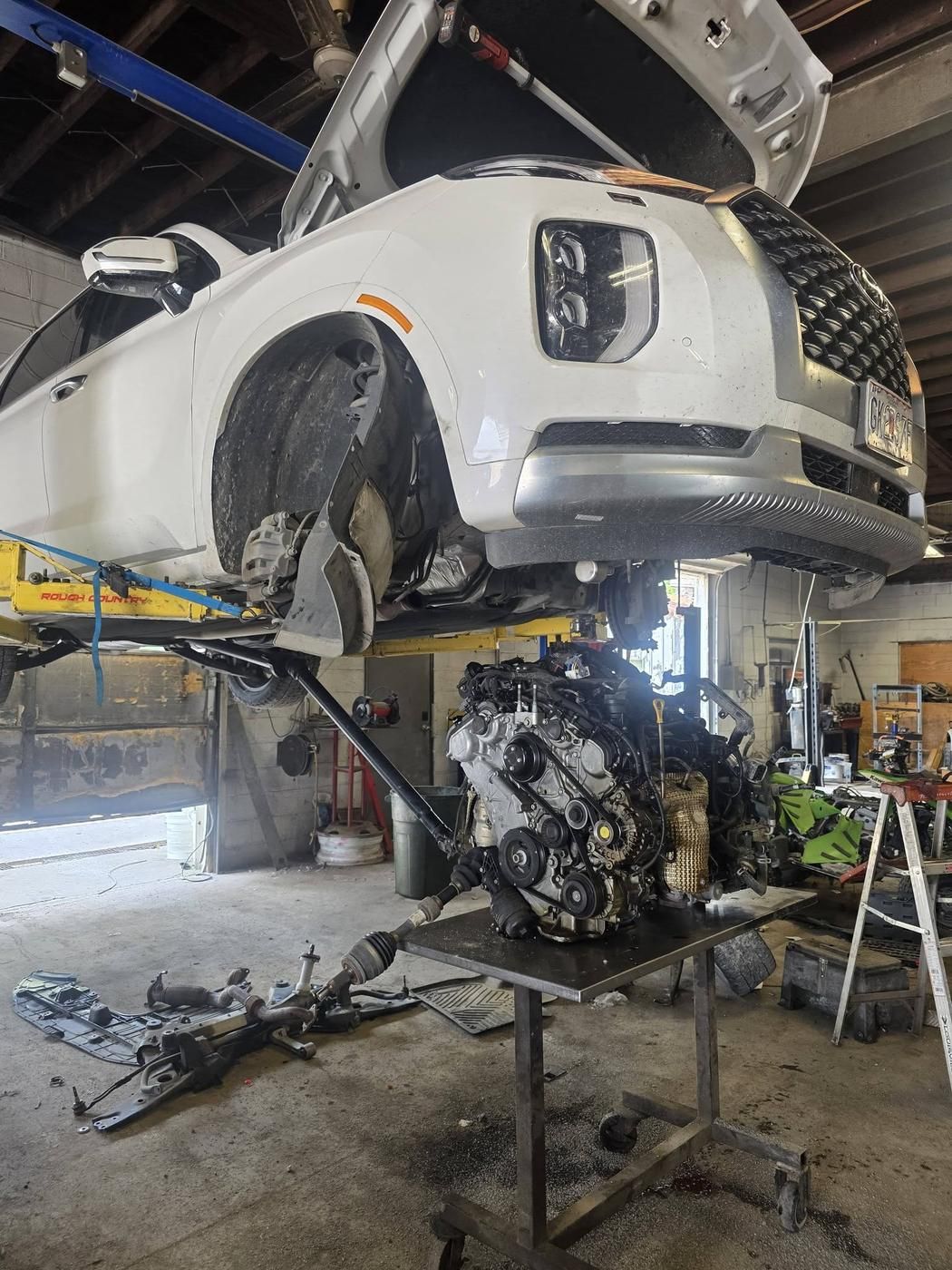 An SUV up on the lift, its engine already out and on the bench below.